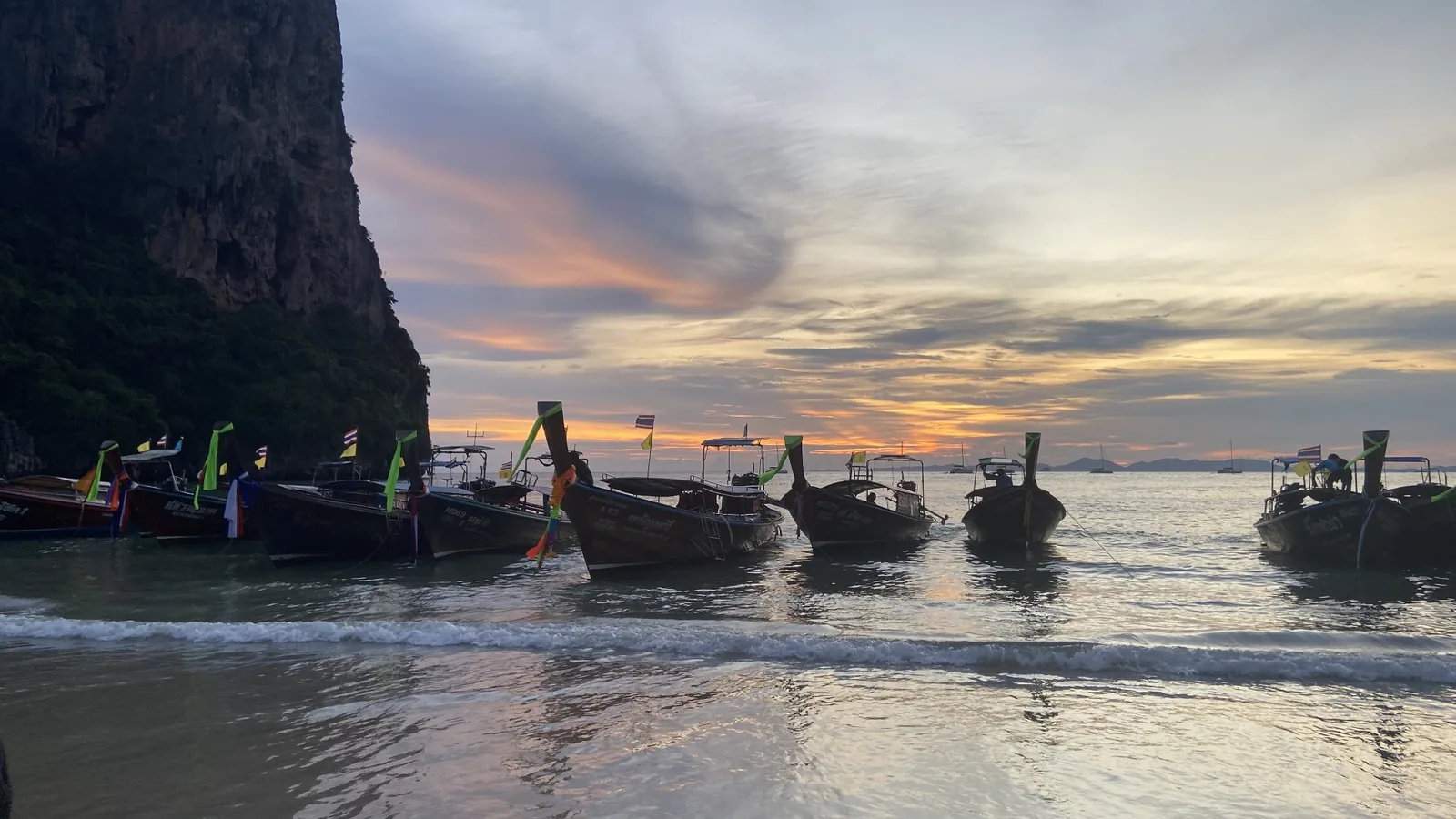 Longtail boats beside a limestone cliff at sunset in Thailand