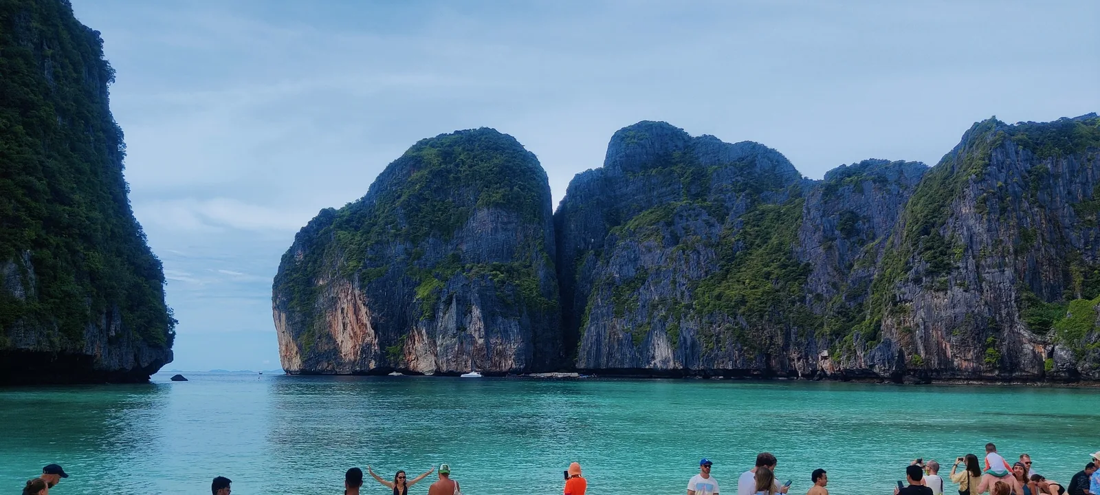 Turquoise water beneath steep limestone cliffs, with visitors along the shore in Thailand